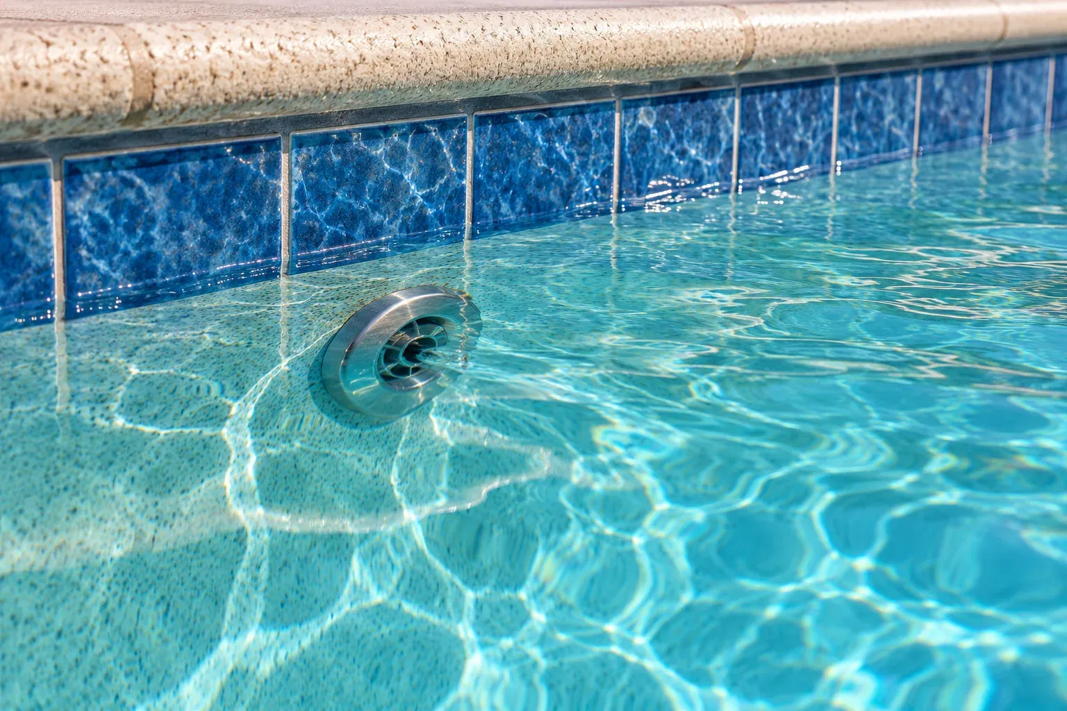 Pool return fitting beneath clear water beside a blue tile waterline
